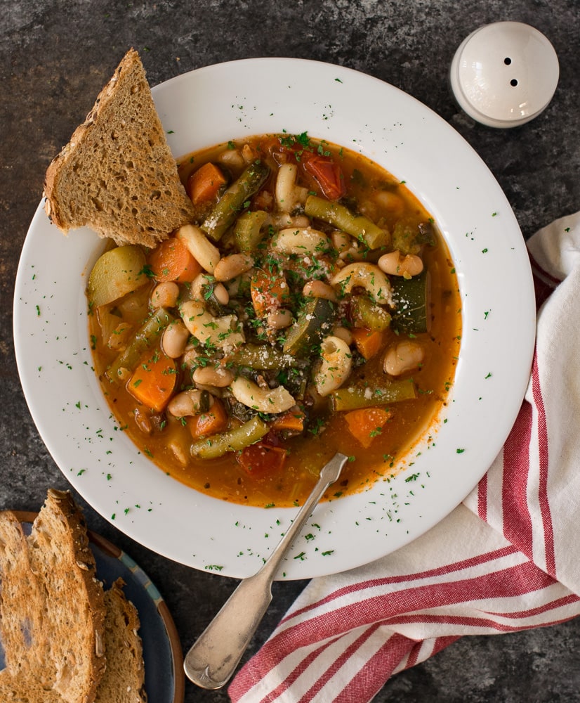 Minestrone soup in a bowl with a side of pepper