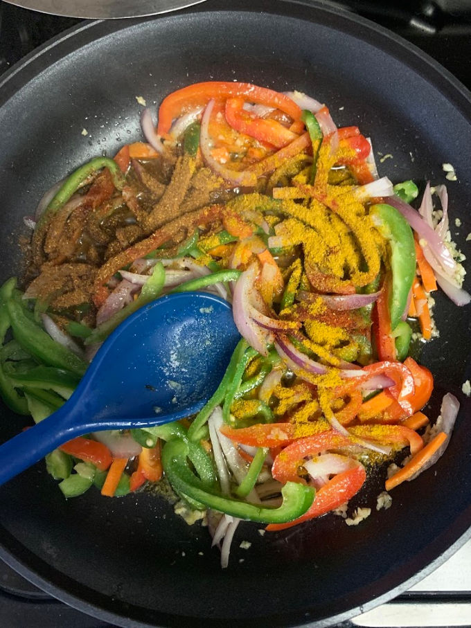 Adding masalas in the pan to cook vegetable jalfrezi.