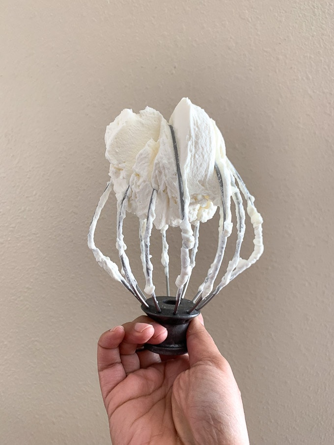 Whipped cream mascarpone frosting held on a whisk after whipping.