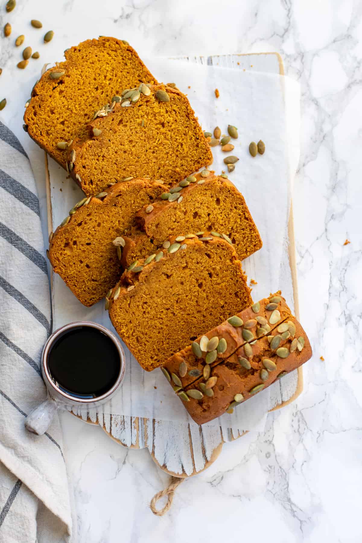 Pumpkin bread sliced and served on a white cutting board with coffee and napkin on the side. 