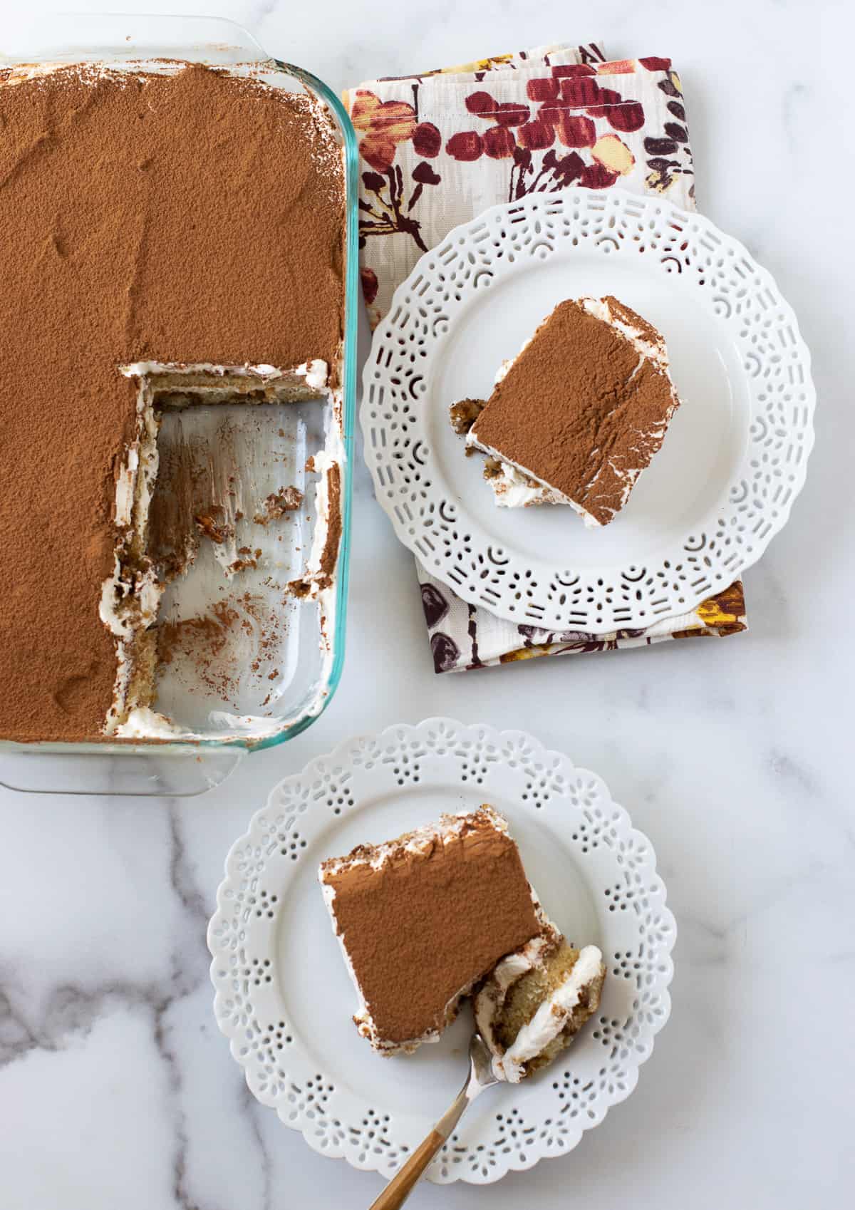 tiramisu served on two white plates with the cake pan on the side.