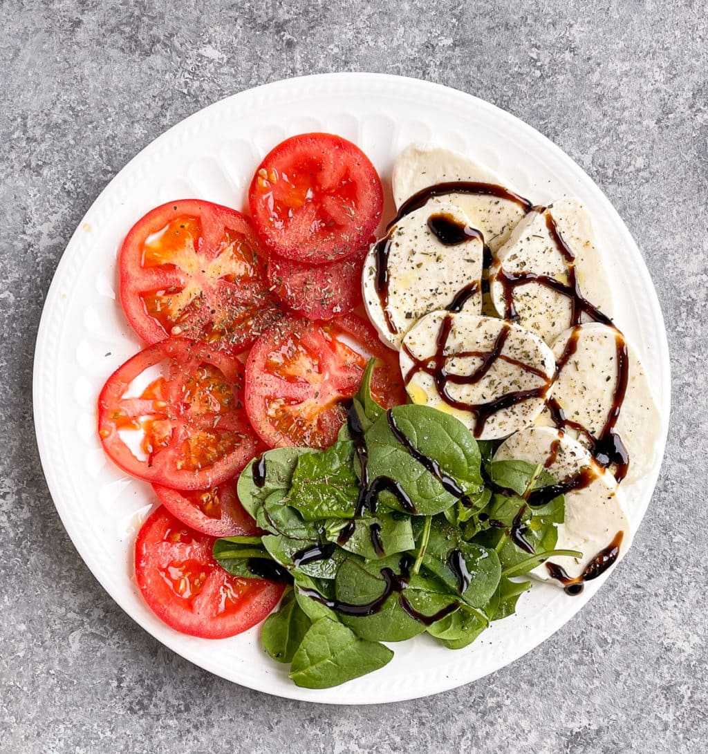 Tomato slices, mozzarella, spinach on a white plate. 
 