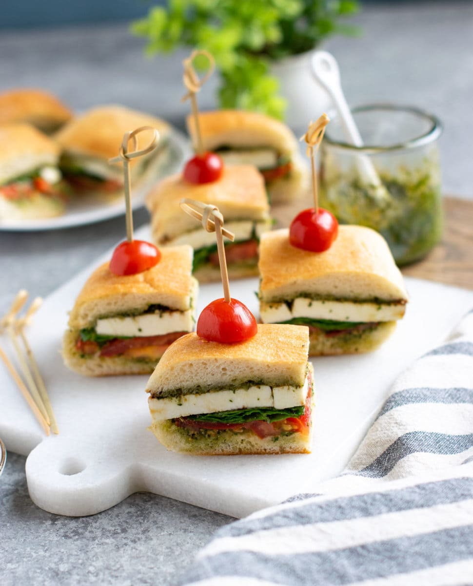 Bite size pesto Caprese sandwiches on a white marble board ready to be served. 