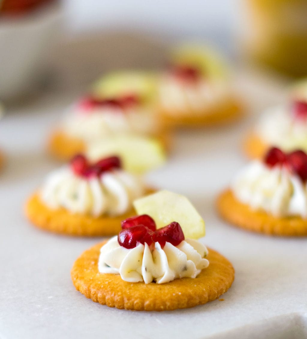 Cream cheese piped on cracker with pomegranate and cucumber on the top. 