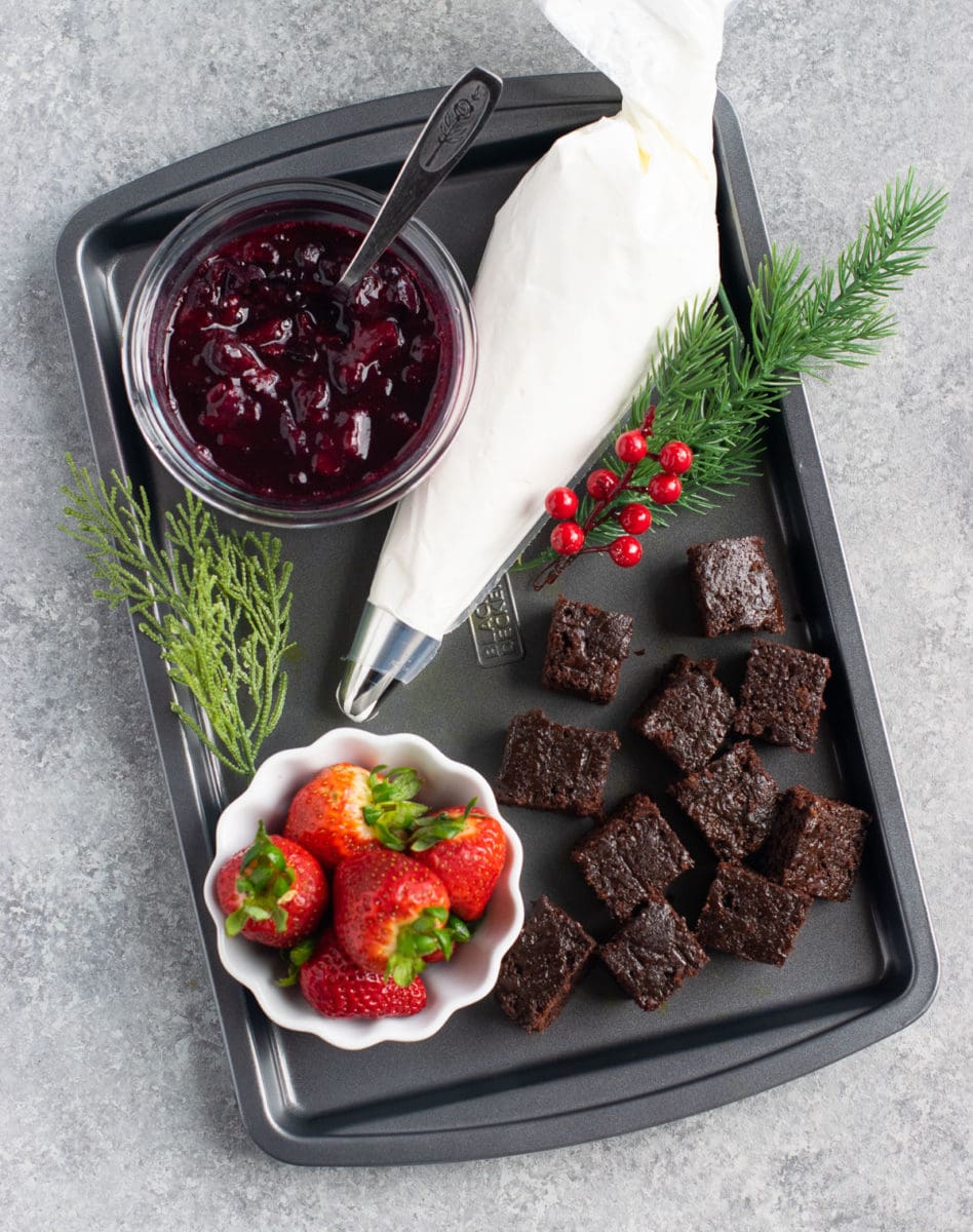 Berry compote, chocolate cake pieces , whipped cream and strawberries on a tray. 