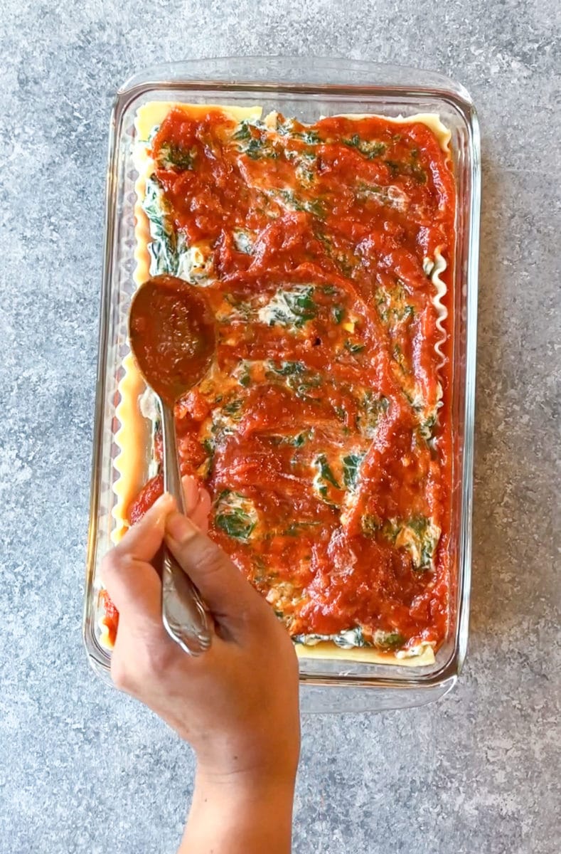 Adding marinara sauce over the spinach ricotta filling with a spoon. 