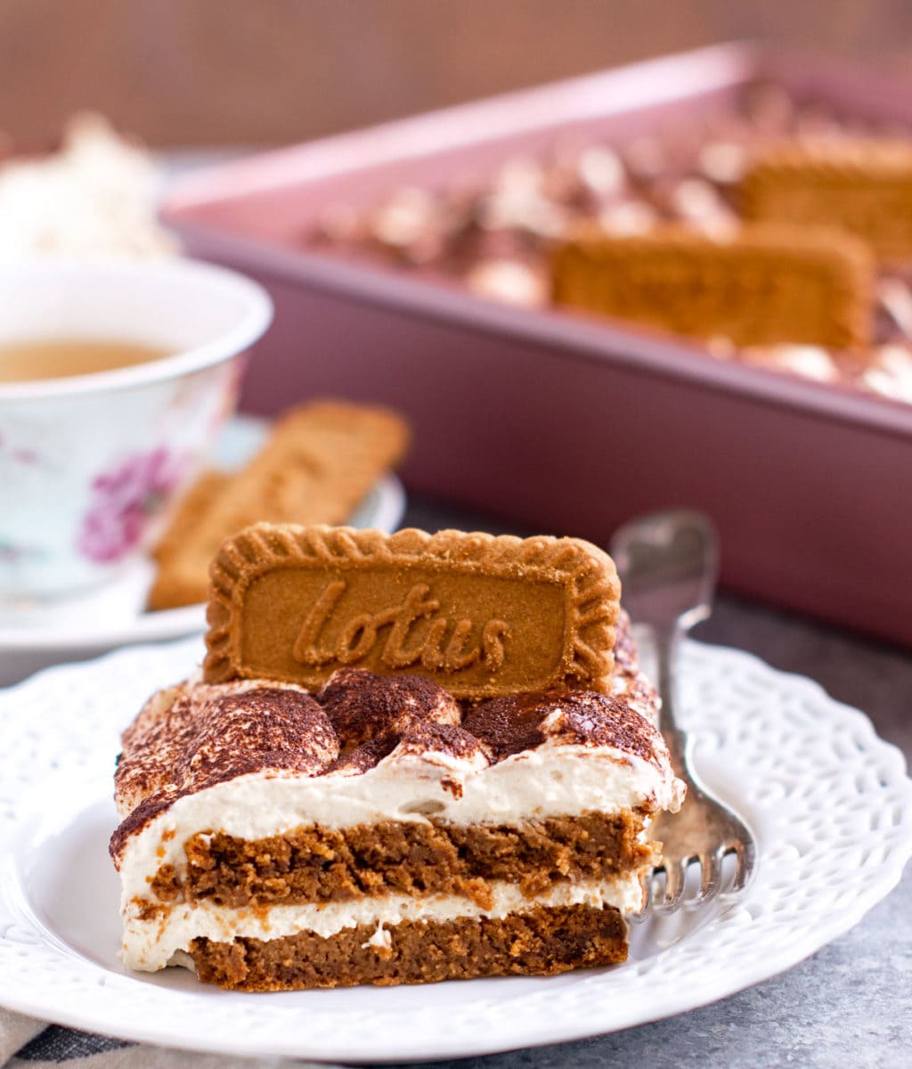 Lotus biscoff tiramisu served on a white plate with a cup of tea on the side. 
