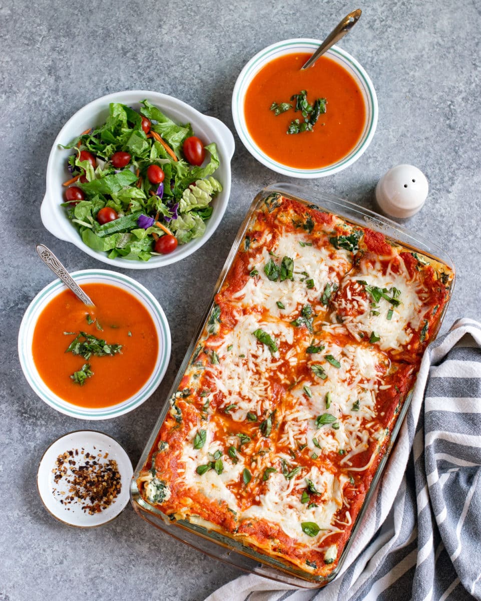 Lasagna casserole served with salad and soup bowls.