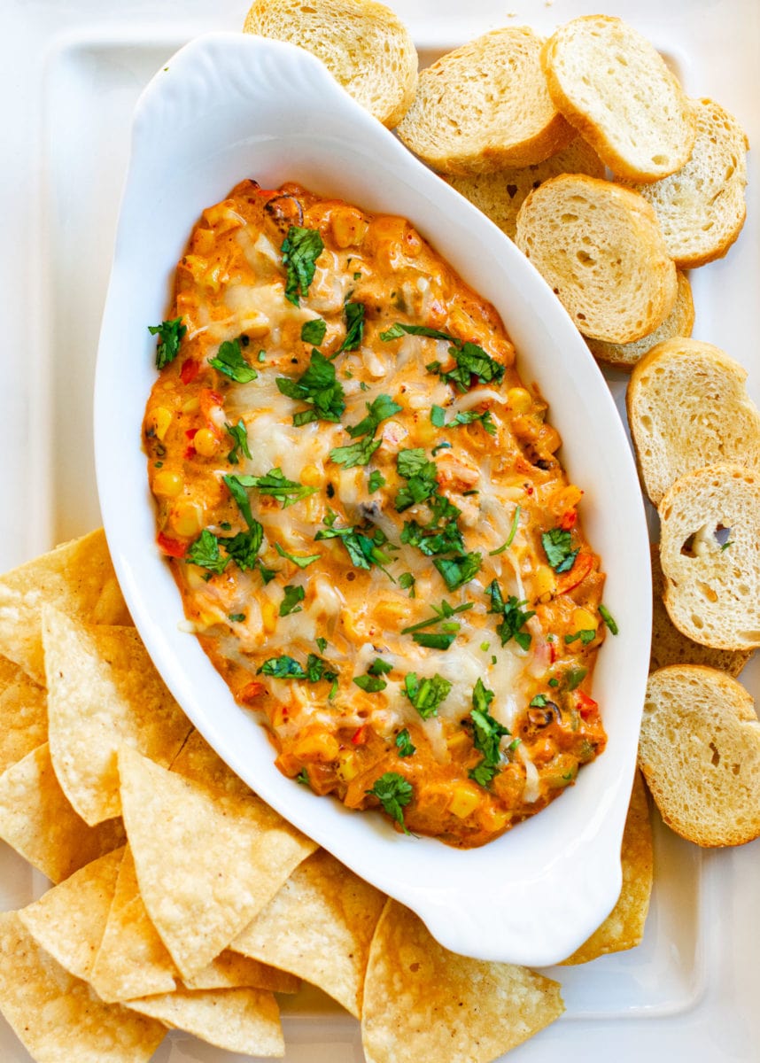 Cheesy corn dip served in a white oval shaped bowl with cilantro on the top. 