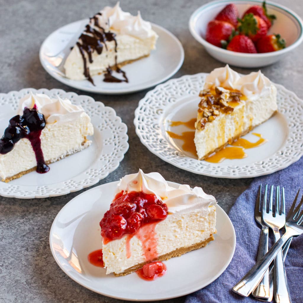 CHEESECAKE SLICES WITH ASSORTED TOPPINGS SET ON WHITE PLATES.