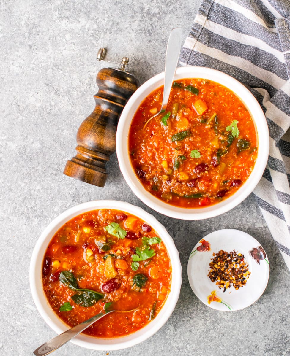 Healthy quinoa minestrone soup served in two white bowls with chili flakes on the side. 
