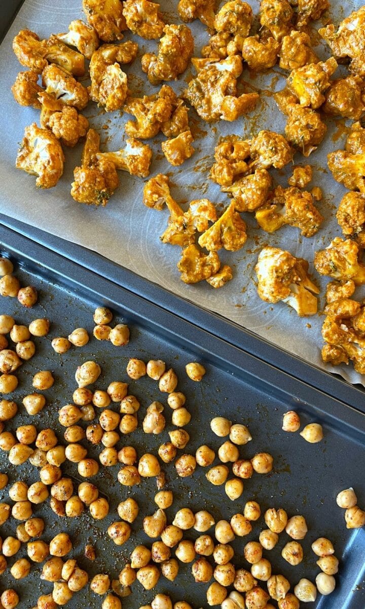 Cauliflower and chickpeas are set on a baking dish, ready to bake. 