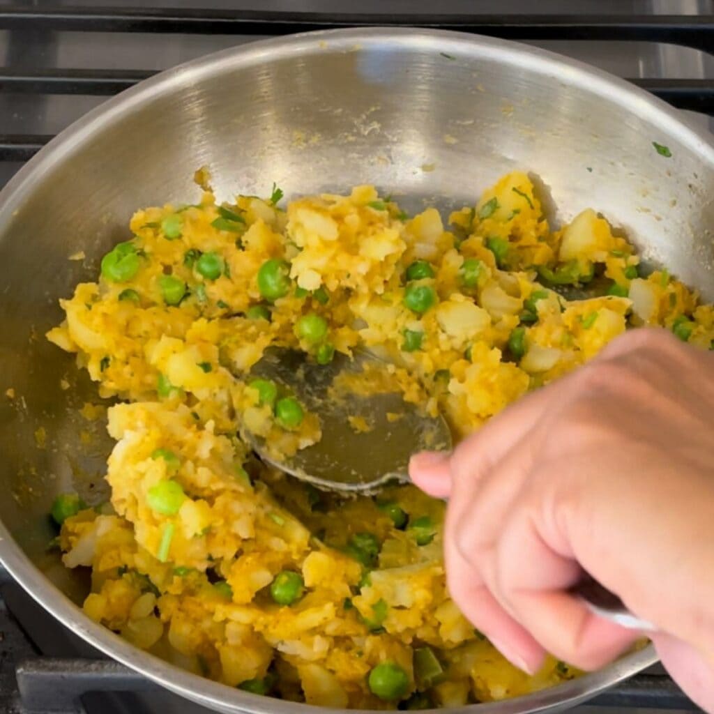 Making the samosa masala in a pan and mashing it with a spoon. 