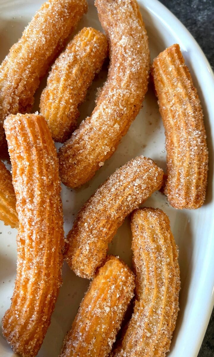 Churros covered in cinnamon sugar set on a oval platter. 