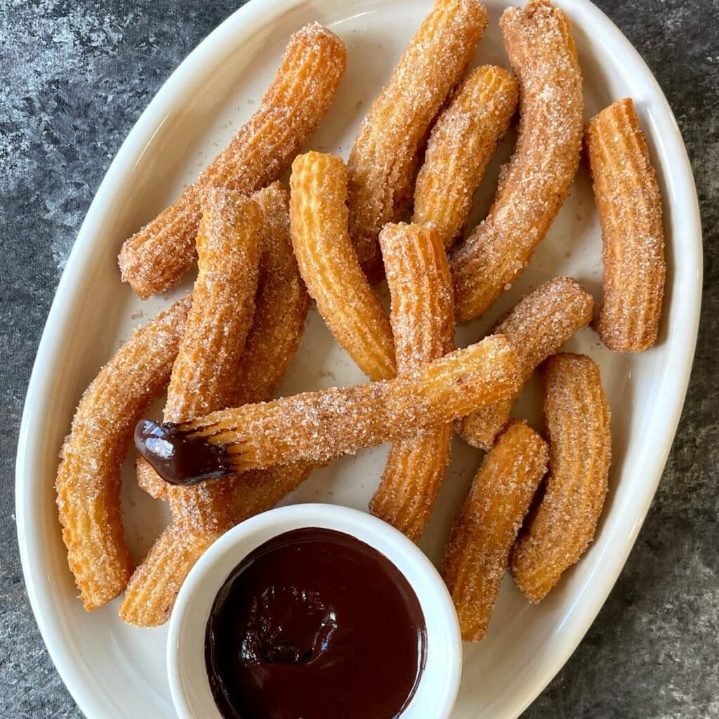 Eggless churros on a white platter with chocolate sauce on the side. 