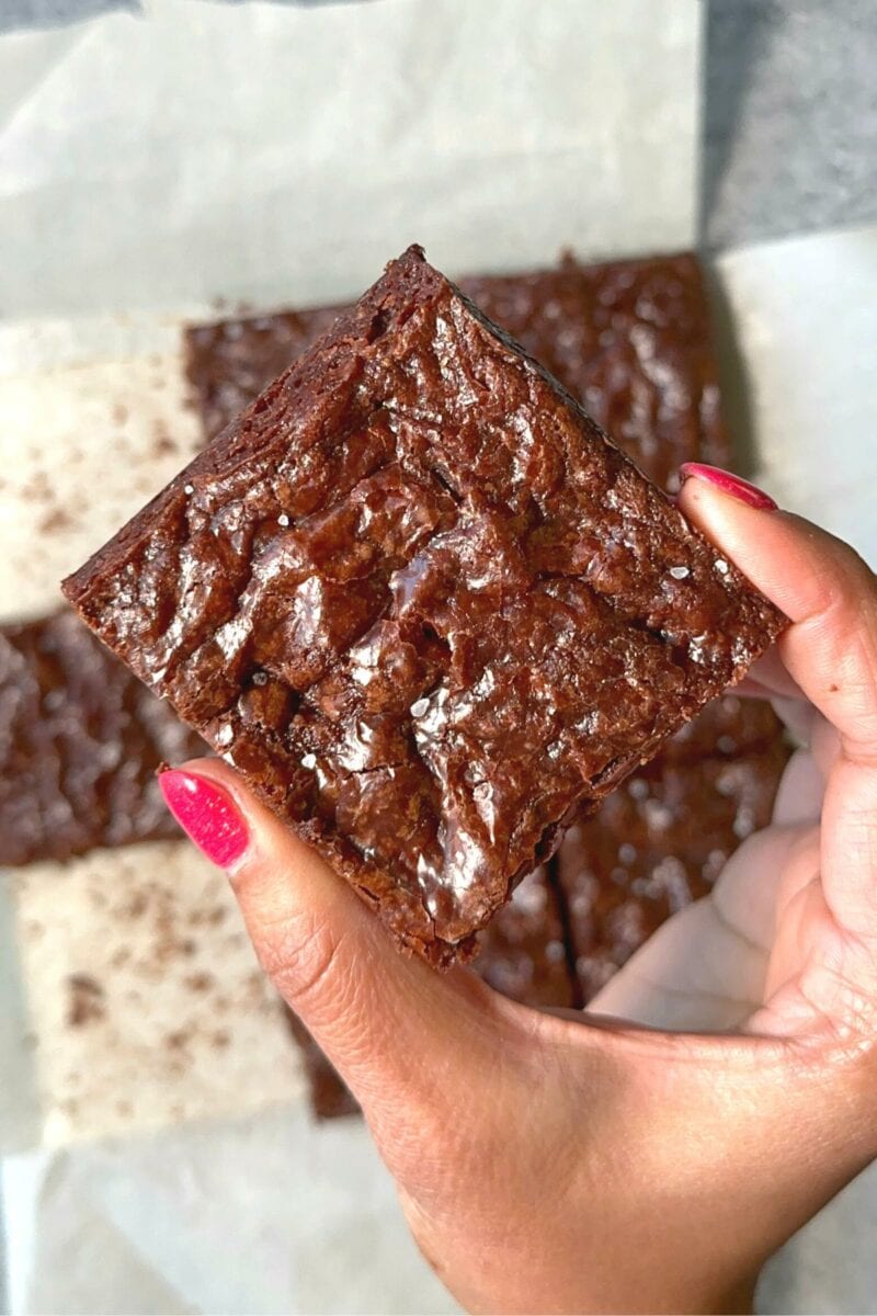 Eggless brownie sprinkled with sea salt on top and held in the hands.