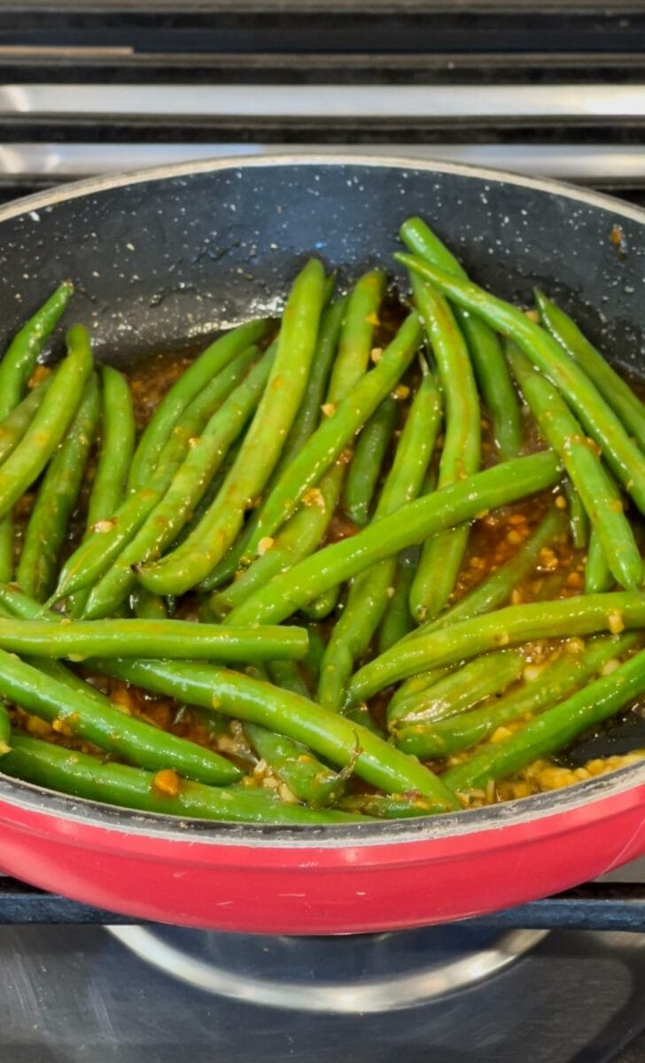 Cooking green beans in a pan with a stir-fry sauce. 