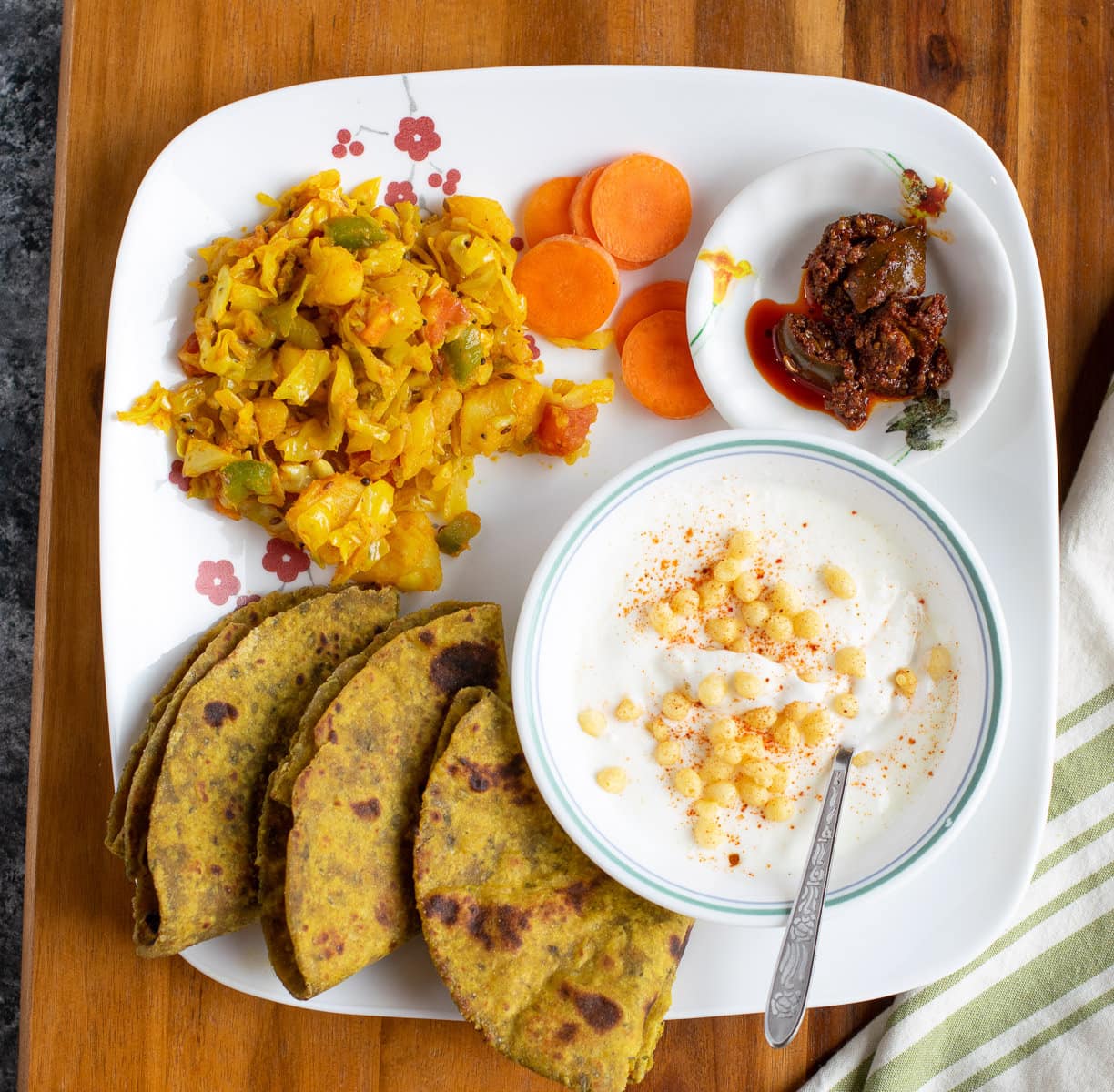 Moong methi theplas on a white plate with gobi suzi, achaar and raita. 